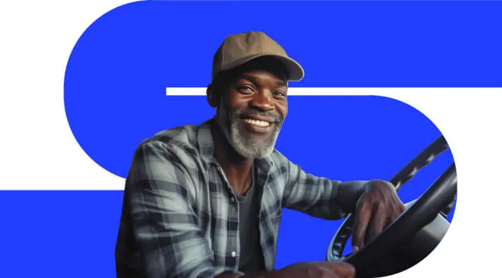 Pessoa utilizando um boné e sorrindo com o braço apoiado em um volante de caminhão